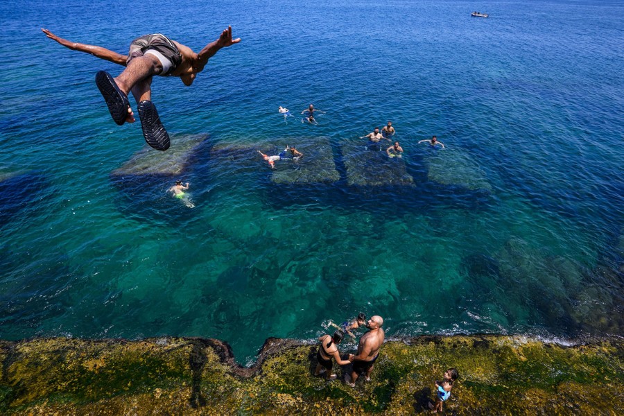 A person makes a high dive into water as others swim below.