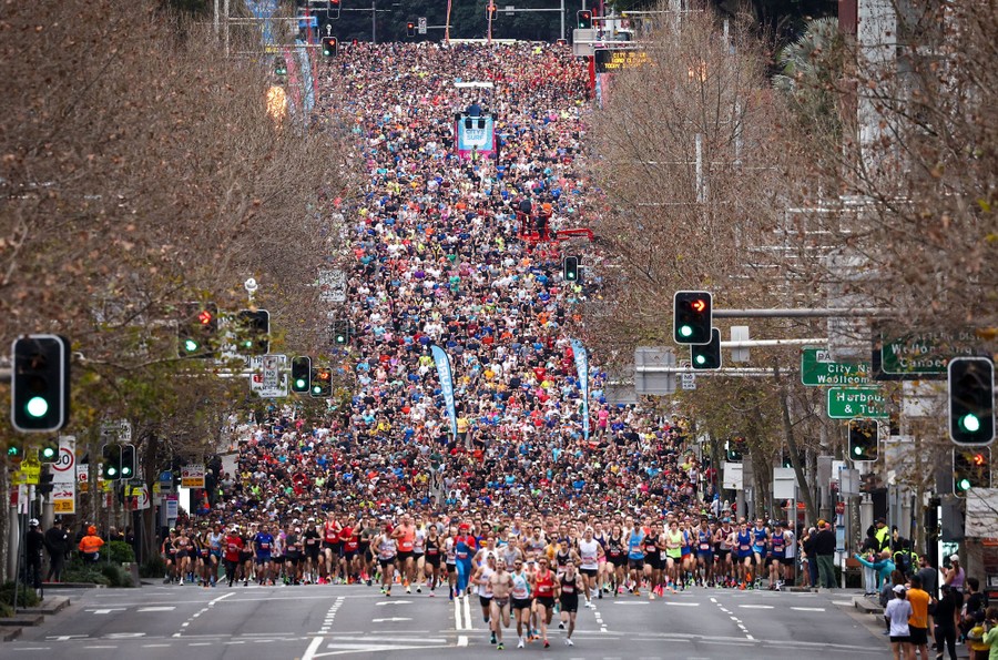 A view down a long and wide city street, of thousands of runners headed toward the camera in a race.