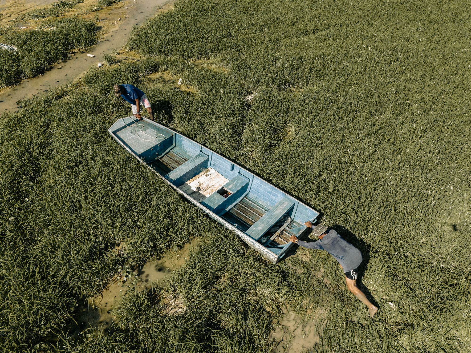 photo from above of two people dragging a metal rowboat across a field of grass