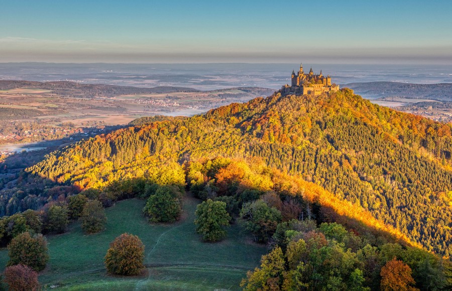 A German castle sits atop a forested mountain.