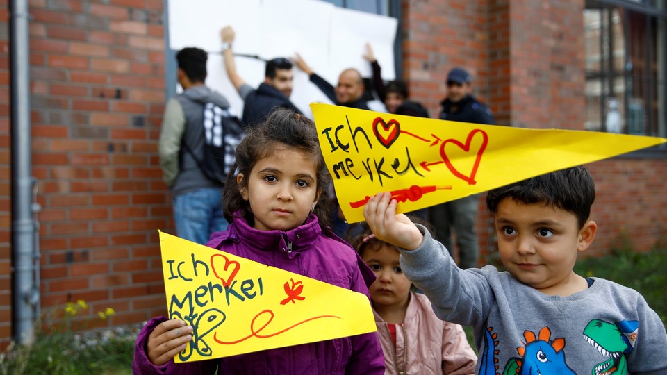 Two Syrian children hold up signs reading "Ich Merkel."