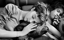 a black and white photo of two girls asleep while sitting, one leaning on the other