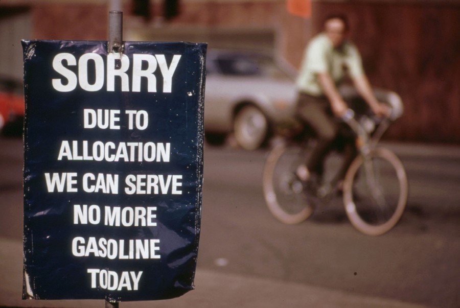 A person rides a bicycle past a sign that says, "Sorry, due to allocation we can serve no more gasoline today."