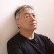 The author Kazuo Ishiguro leaning against a wall with two paintings visible