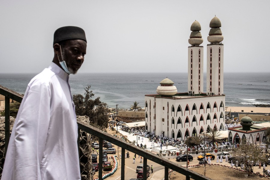 A man looks over. balcony, with a mosque visible in the background.