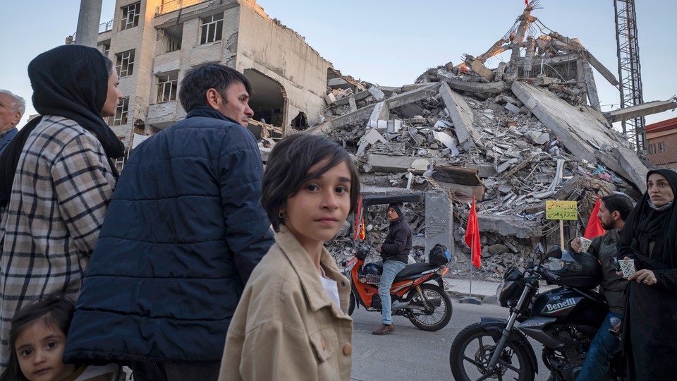 People including two young girls standing in front of rubble in a residential area in Tehran