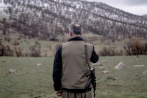 A man stands with his rifle, facing a mountain range.