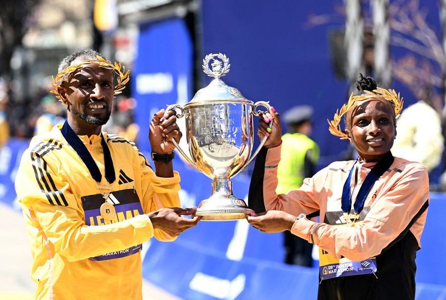 Two runners hold up a large trophy together at a finish line.