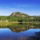 A short mountain stands beyond a lake, surrounded by trees, in Maine's Acadia National Park