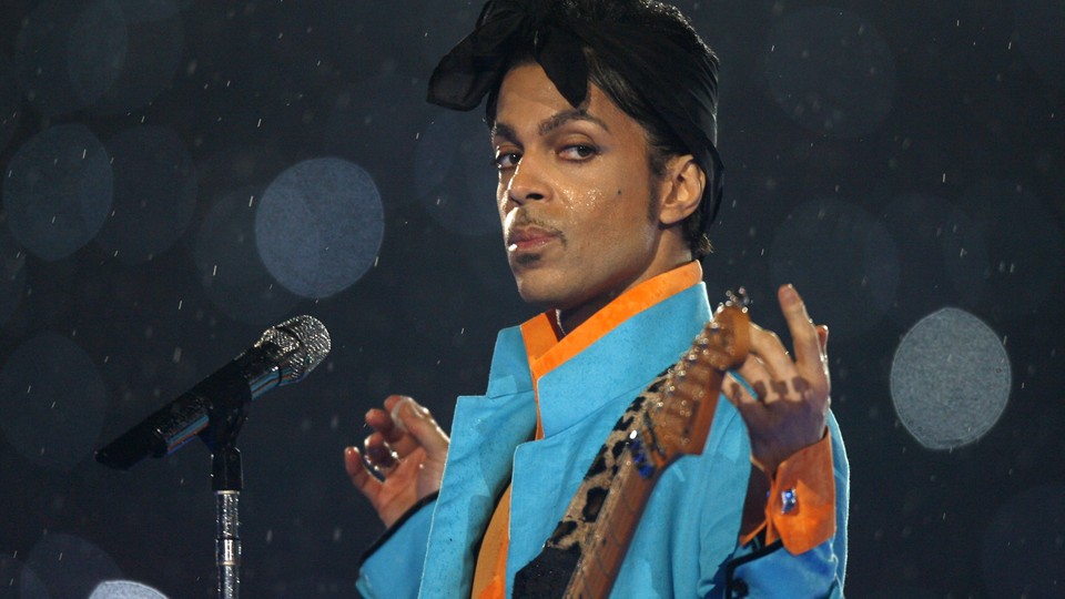 Prince standing at a microphone, holding a guitar, in the rain.