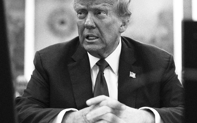 Black-and-white photo of Donald Trump in a suit siting with his hands crossed in front of him