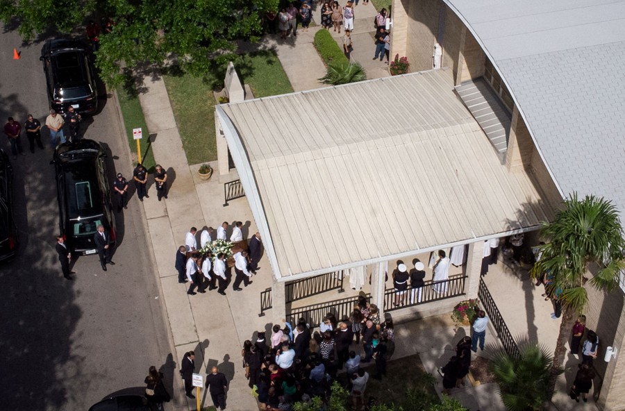An aerial view of a funeral with pallbearers carrying a casket into a building