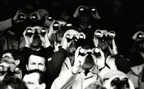 A black-and-white photograph of several men holding binoculars up to their faces to look at something far away