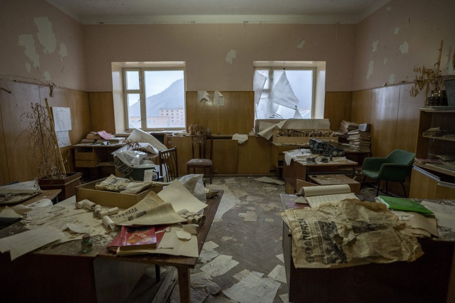 A view inside an abandoned office, showing papers and belongings scattered among several desks.