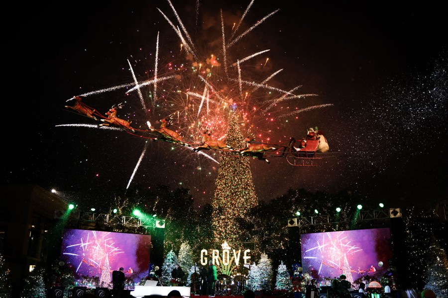 Santa's sleigh and fireworks appear above a tall Christmas tree in front of a stage.