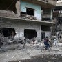 A boy rides his bicycle past the rubble of bombed-out buildings.