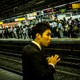 A Japanese man stands in a crowded subway station.