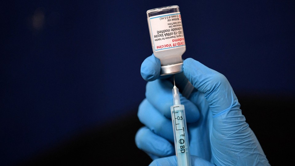 An image of a pair of gloved hands inserting a syringe into a vaccine vial