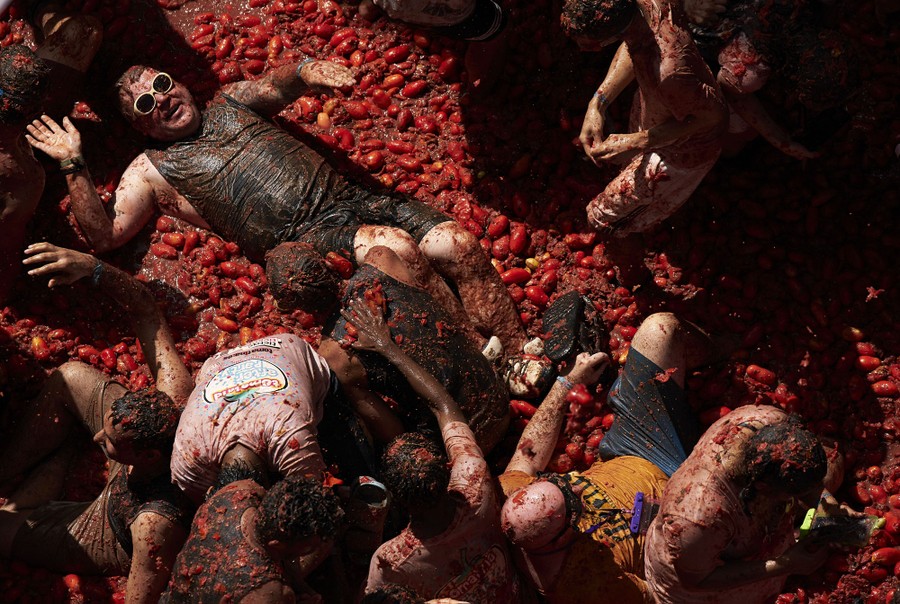 People wade and lie down in a pile of pulped tomatoes.