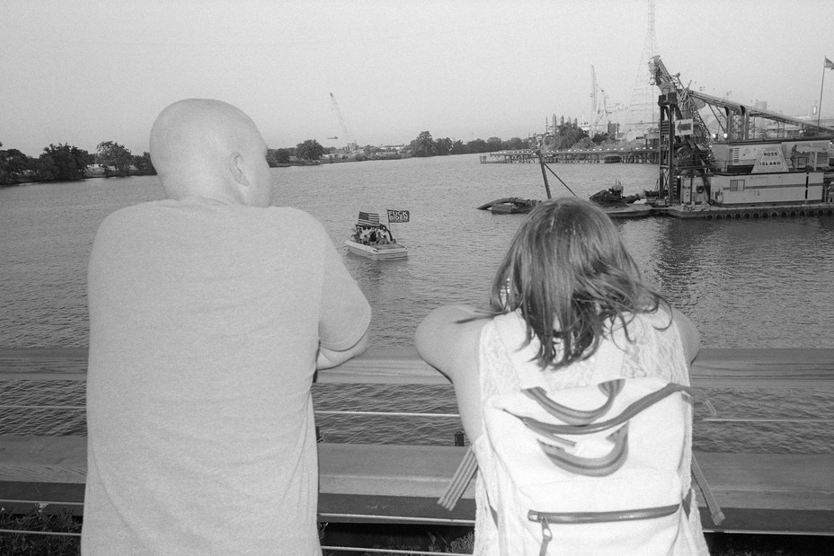 people look out over the water where a boat with a flag is floating.