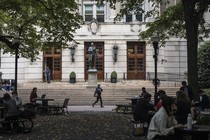 A photo of people sitting at tables in a leafy courtyard in front of a building on Columbia University's campus