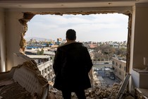 Photograph of a man looking through the side of a bombed out building.