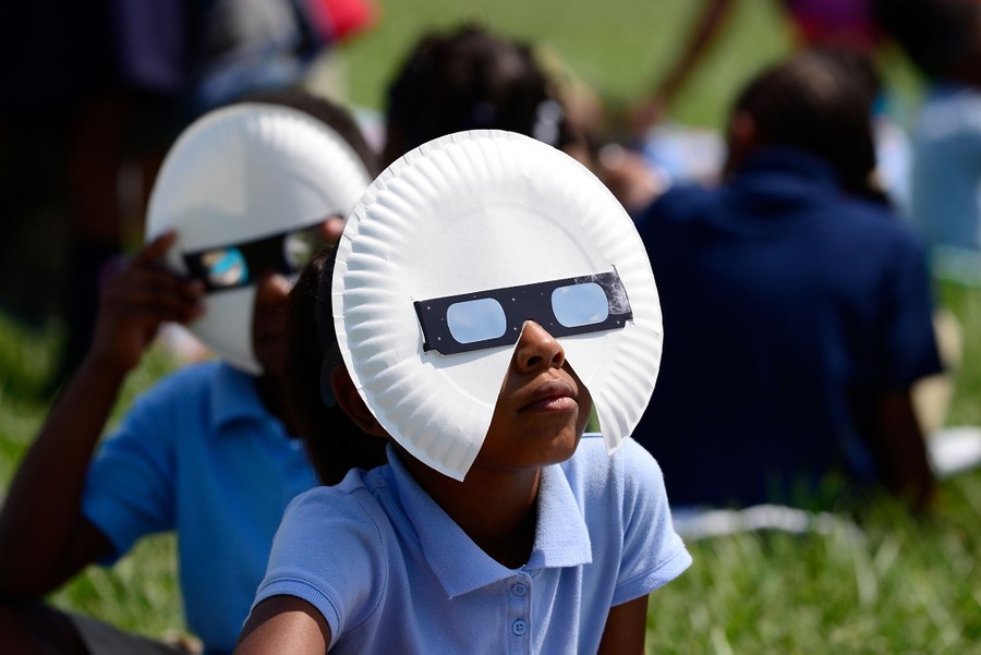 Young people wearing eclipse glasses and paper-plate masks view an eclipse.