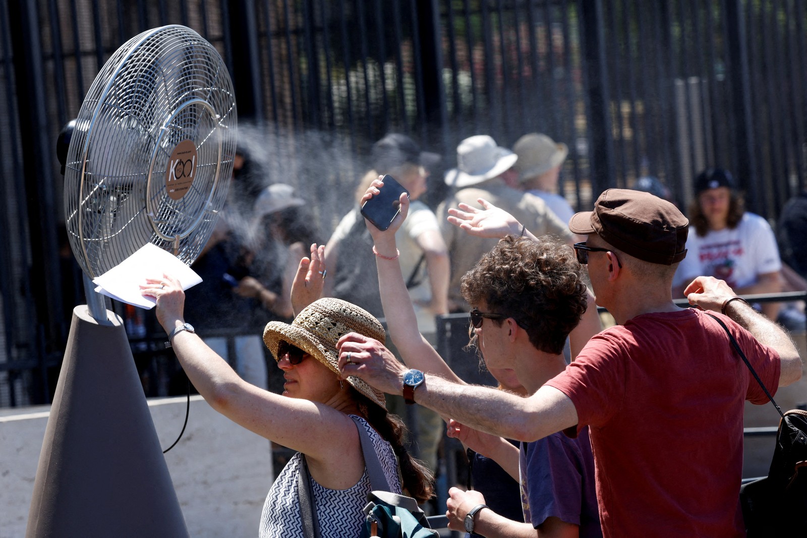 Tourists stand in front of a cooling fan.
