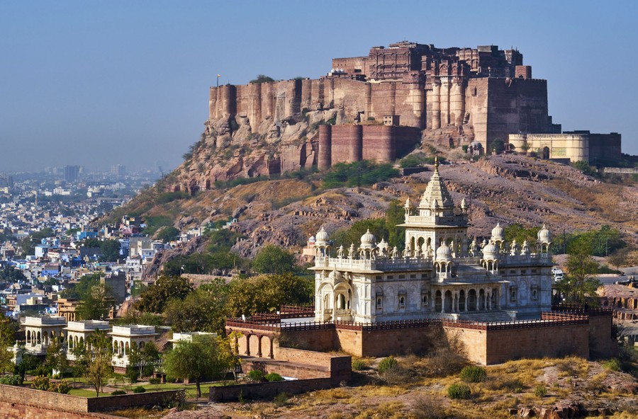 A large fortress stands on a rocky outcrop above a nearby city.