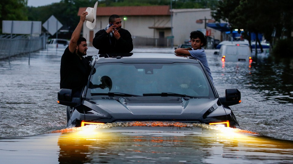 Three people hang onto the outside of a truck as it travels through floodwaters in Houston.