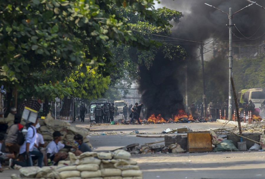 Protesters take cover behind a makeshift barricade on a road as armed security forces approach.