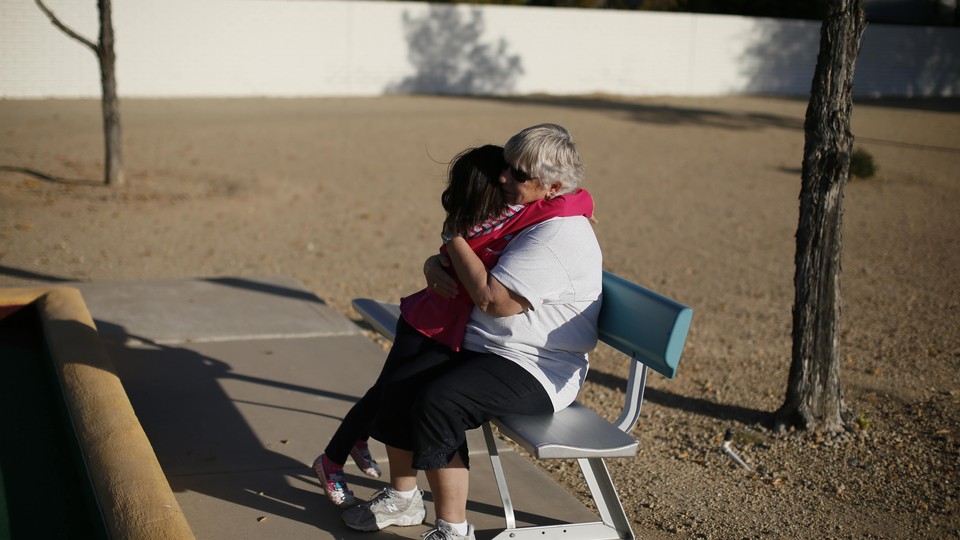 A young child hugs an older person sitting on a park bench.