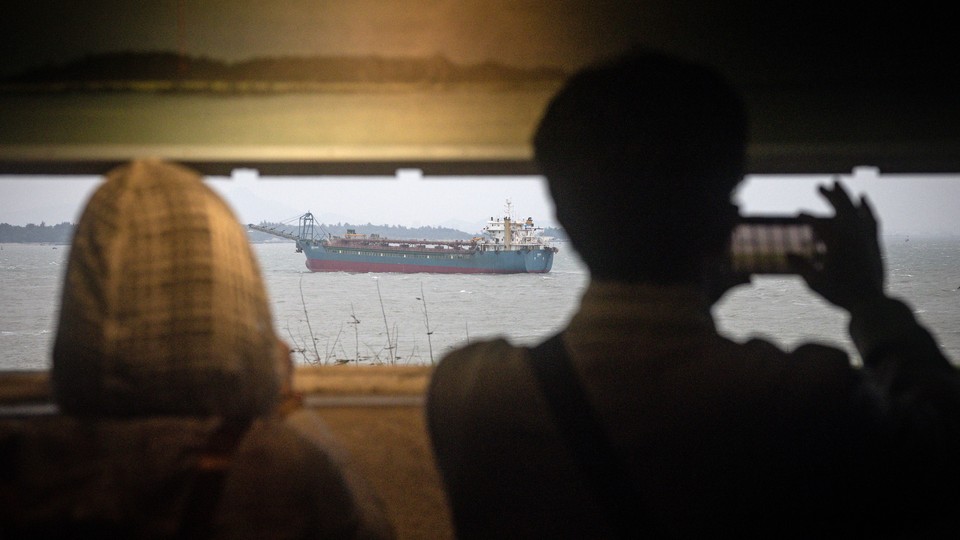 Two tourists, seen from behind, taking a photo of the Chinese mainland and Chinese flagged sand dredgers from the bunker of an old Taiwan military observatory in Kinmen, Taiwan.