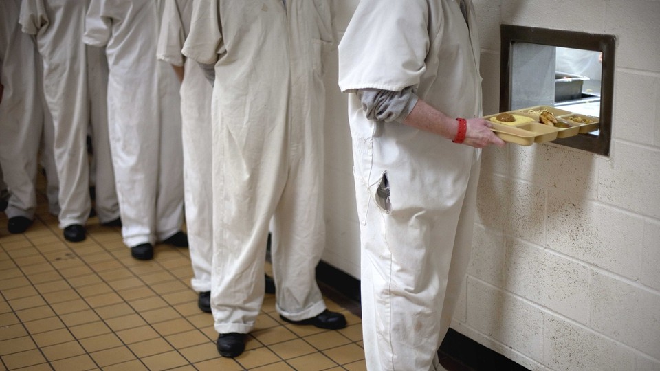 Inmates line up to receive lunch trays through a hole in a cafeteria wall.