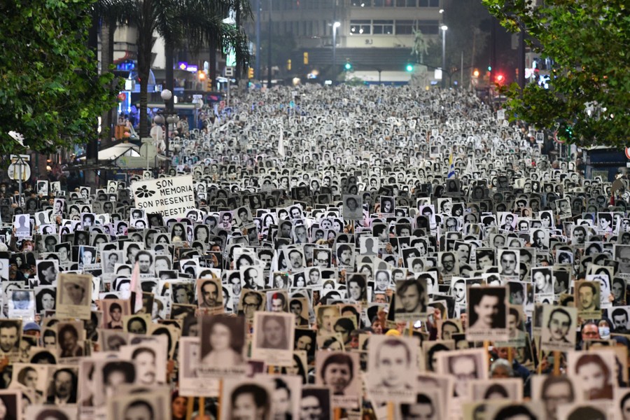 A large crowd of people march in a street, carrying portraits of people above their heads.