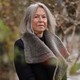 A portrait photo of Louise Glück in black coat standing outside among bare branches