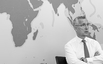 Jens Stoltenberg sits with his arms folded in front of a map of the world.