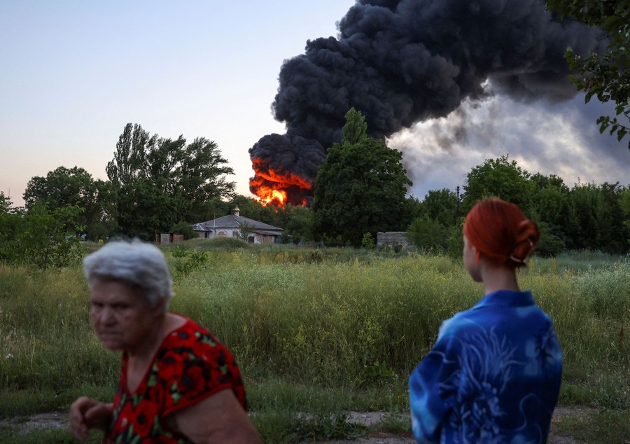 Two people look at a distant fire and column of smoke near a residential area.