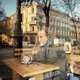 a portrait of Rod Dreher, wearing a gray coat and large scarf, sitting at a cafe table in Budapest