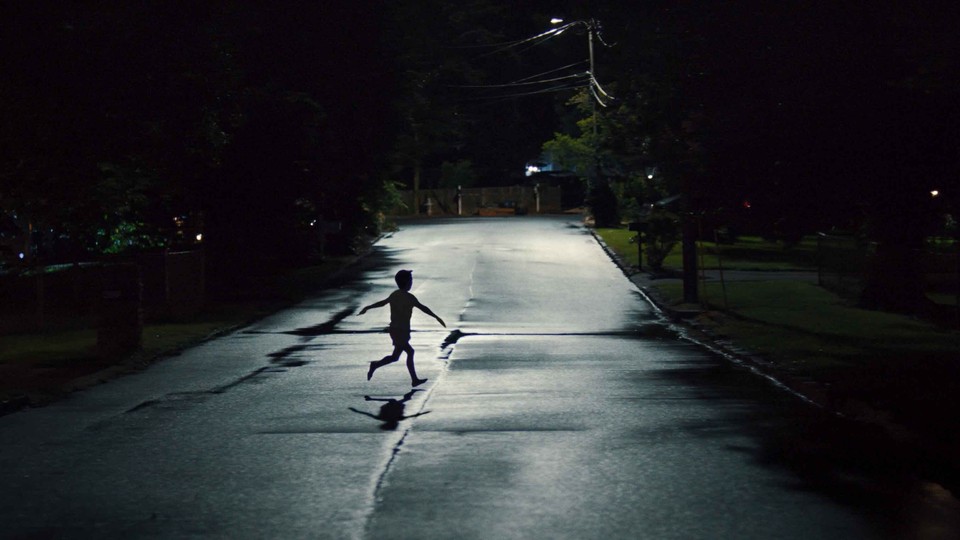 a child runs through a street at night, his arms outstretched