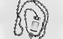 A black-and-white rosary that ends with a vaccine bottle
