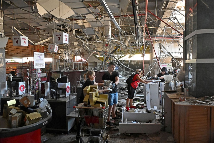 Several people work inside a heavily damaged supermarket, moving small items and clearing debris.