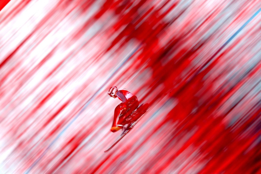 A skier races down a hill in a blur, sitting in a fiberglass seat attached to a ski.