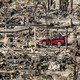 A single undamaged red car sits in a ruined neighborhood after a fire.