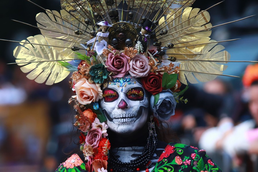 A person wears a Catrina costume, including an ornamental headpiece and detailed skull makeup.
