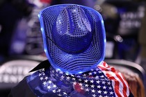 A color photograph of a person in a sparkly blue cowboy hat with an American flag draped around their shoulders, seen from the back.
