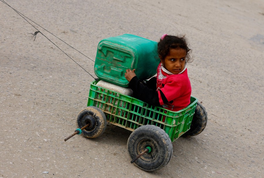 A girl sits in a cart made from a plastic crate and wheels.