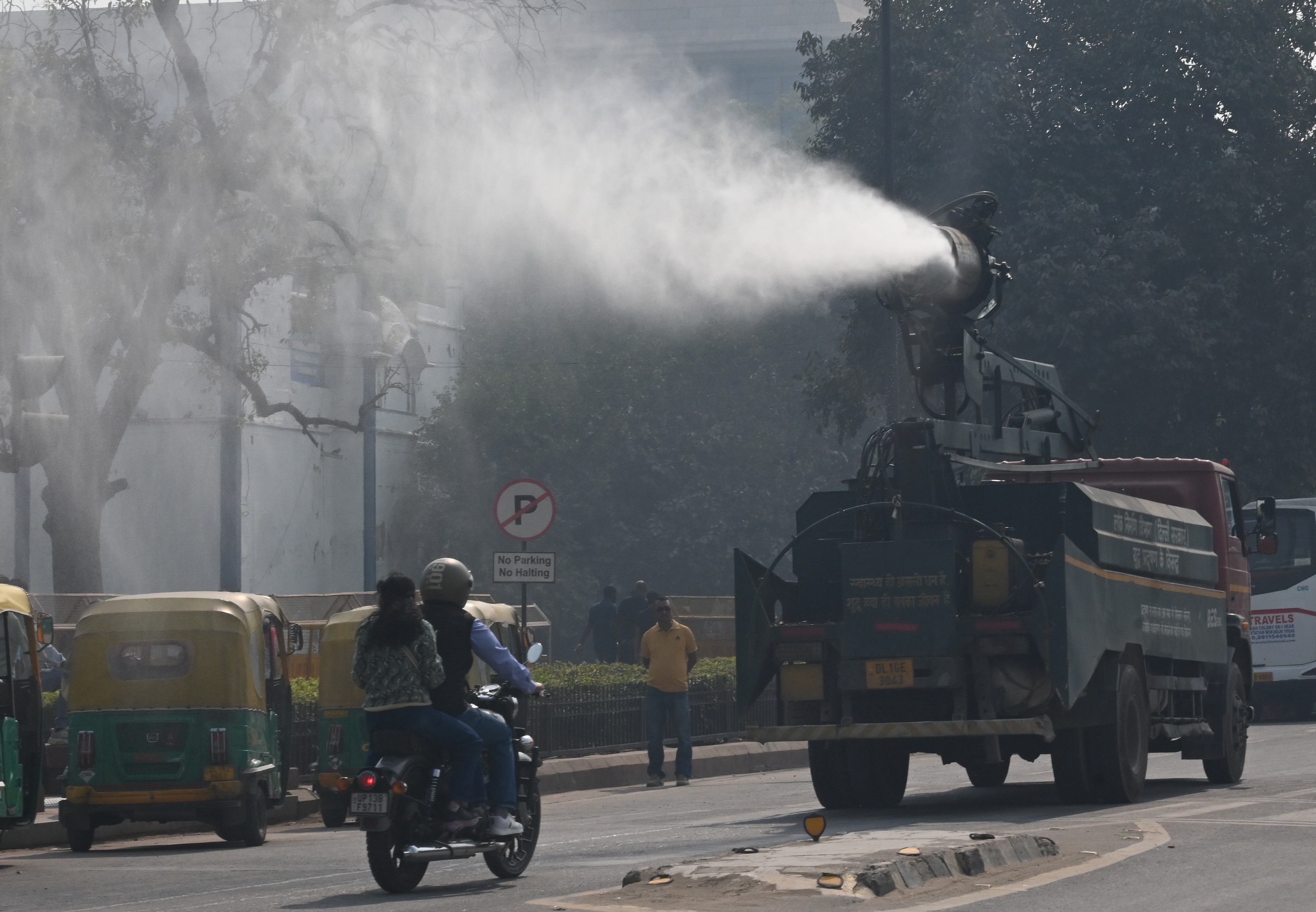 A device mounted to the top of a truck sprays a mist of water in the air as it drives down a road.