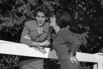 Black and white photo of two women gossiping across a fence