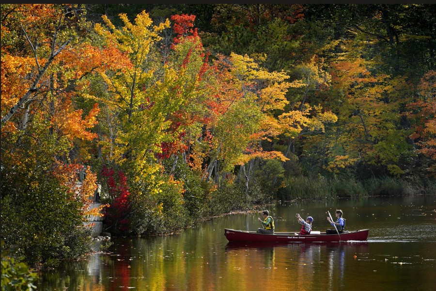A passenger in a canoe photographs fall foliage.